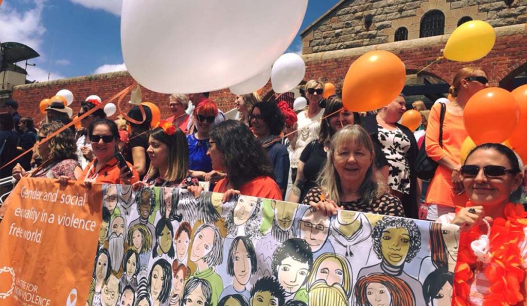 People standing behind banner holding balloons at White Ribbon Day march