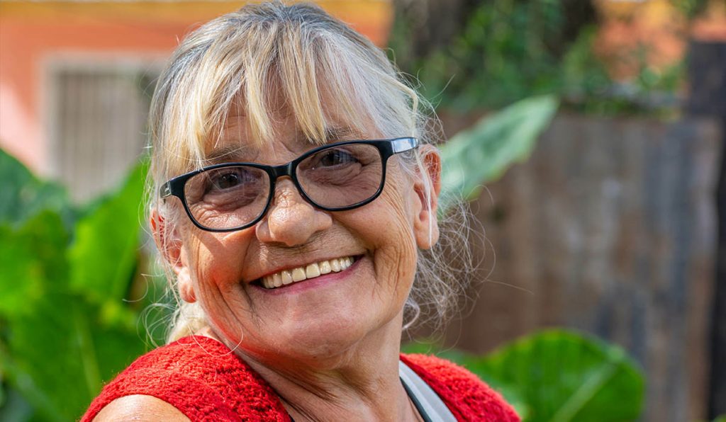 Woman with red top and black glasses smiling at camera in garden