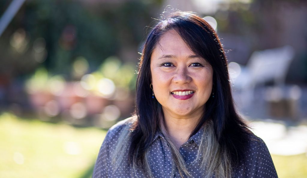 Woman with dark hair smiling at camera with blurred outdoor background
