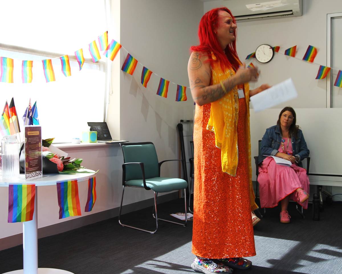 Starlady wearing bright orange colours speaking in front of rainbow flags